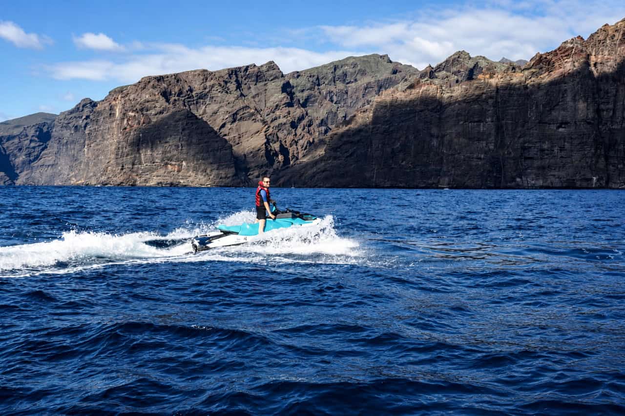 Jet ski rider speeding across the water along the rugged volcanic coastline near Los Gigantes, Tenerife.