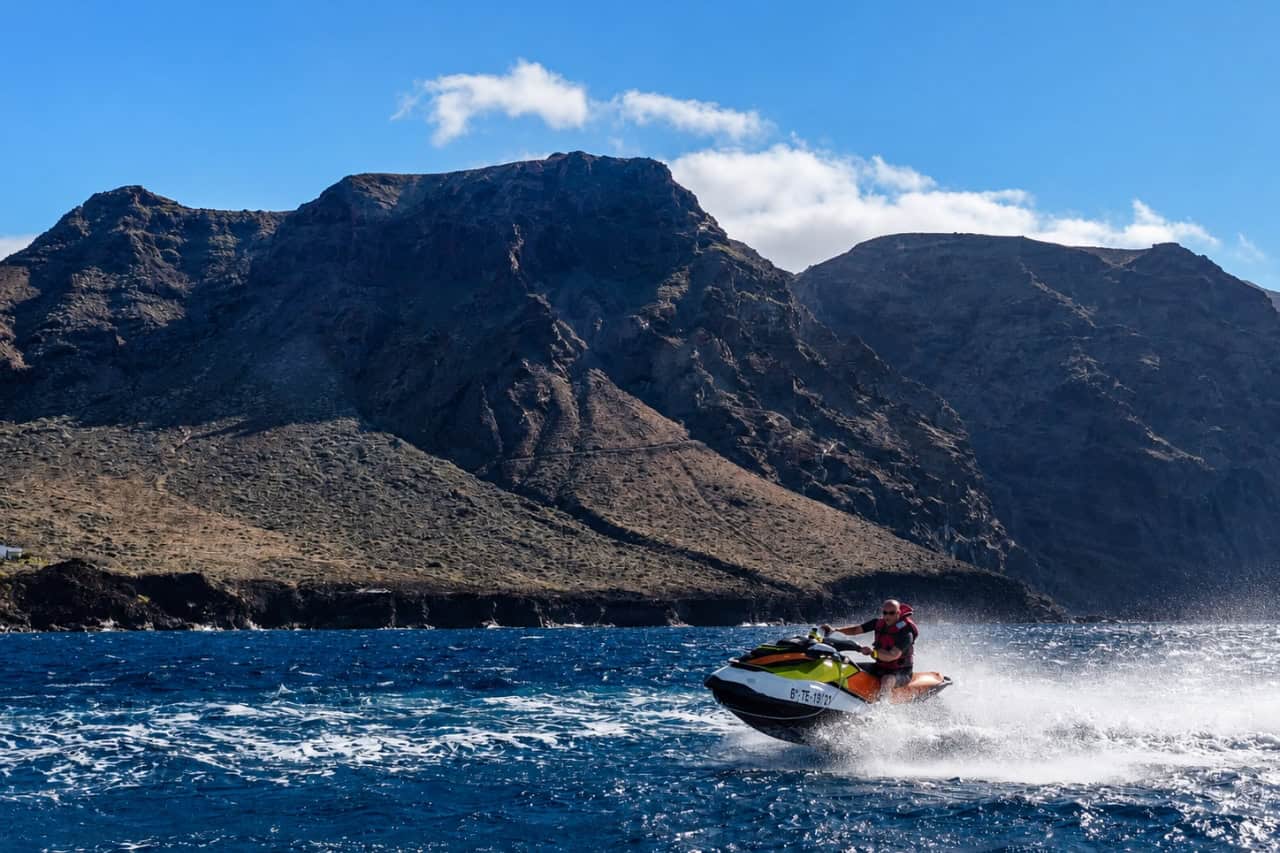 Man riding a Sea-Doo jet ski across the ocean with the Los Gigantes cliffs in the background.