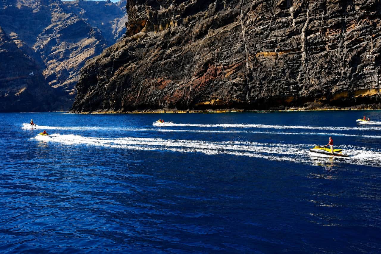 Several jet skis riding across the Atlantic Ocean beside the dramatic Los Gigantes cliffs in Tenerife.