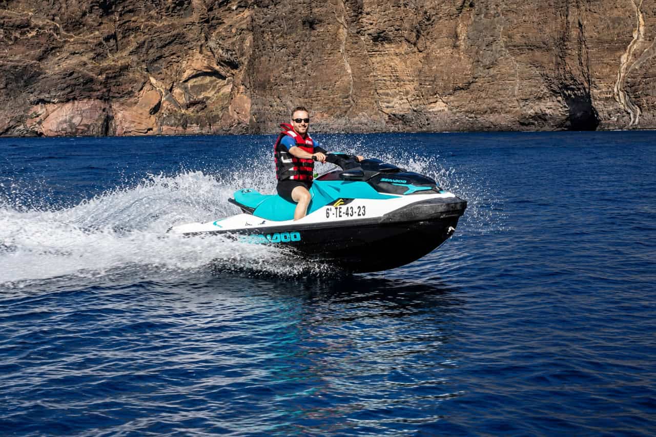 Rider on a jet ski cruising along the coast beneath the towering Los Gigantes cliffs in Tenerife.