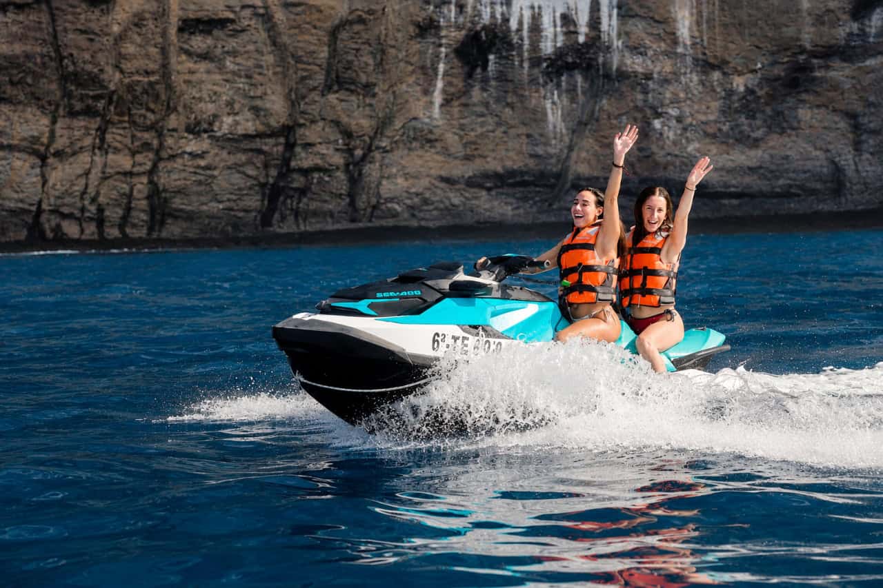 Two women raising their hands while riding a Sea-Doo jet ski near Los Gigantes in Tenerife.