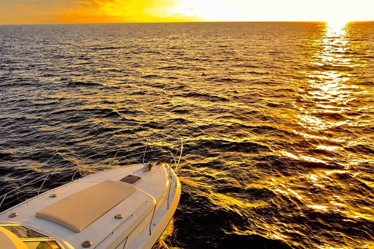 La proa de un barco privado frente a una dorada puesta de sol atlántica en Tenerife, con una cálida luz vespertina reflejándose en el mar.