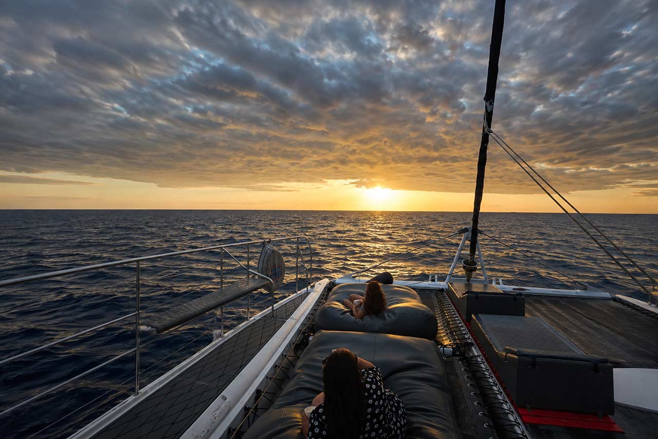 Gasten die ontspannen op comfortabele zitzakken aan boord van de catamaran White Tenerife terwijl ze genieten van de zonsondergang boven de Atlantische Oceaan