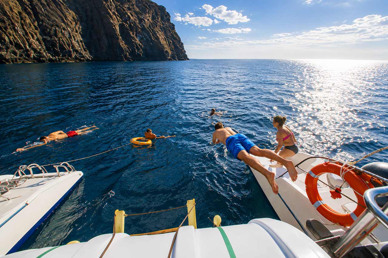 Een gast die tijdens een zwempauze op de catamaranexcursie White Tenerife langs de kust van Tenerife in de Atlantische Oceaan springt
