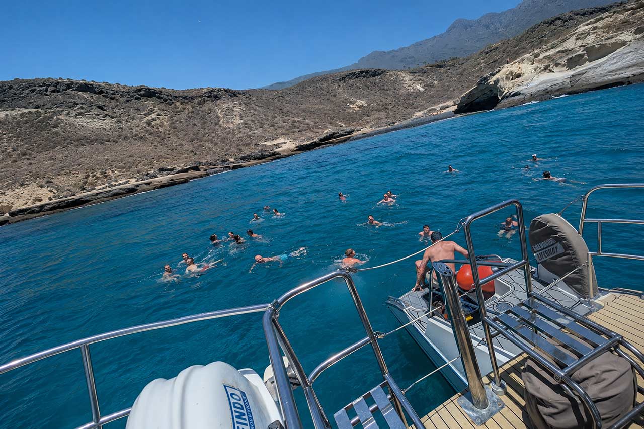 Gasten die tijdens de boottocht White Tenerife in het heldere water van de Atlantische Oceaan zwemmen langs de vulkanische kustlijn van Tenerife
