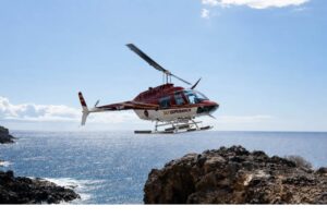 Red helicopter flying above Tenerife’s volcanic coastline and Atlantic Ocean during a scenic helicopter tour.