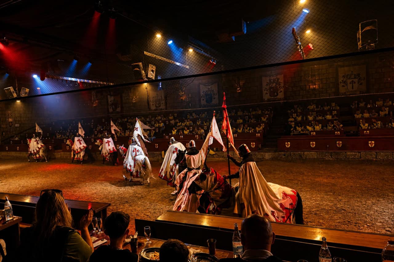 Mounted knights carrying flags ride through the arena as families watch the family medieval show Tenerife.