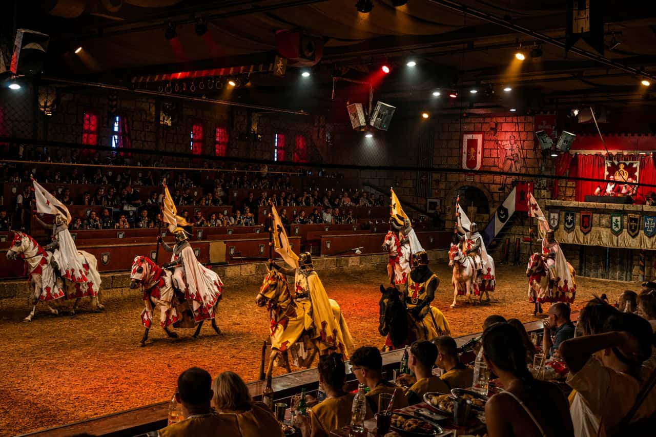 Mounted knights carrying coloured team flags cross the arena during a knights tournament Tenerife performance.