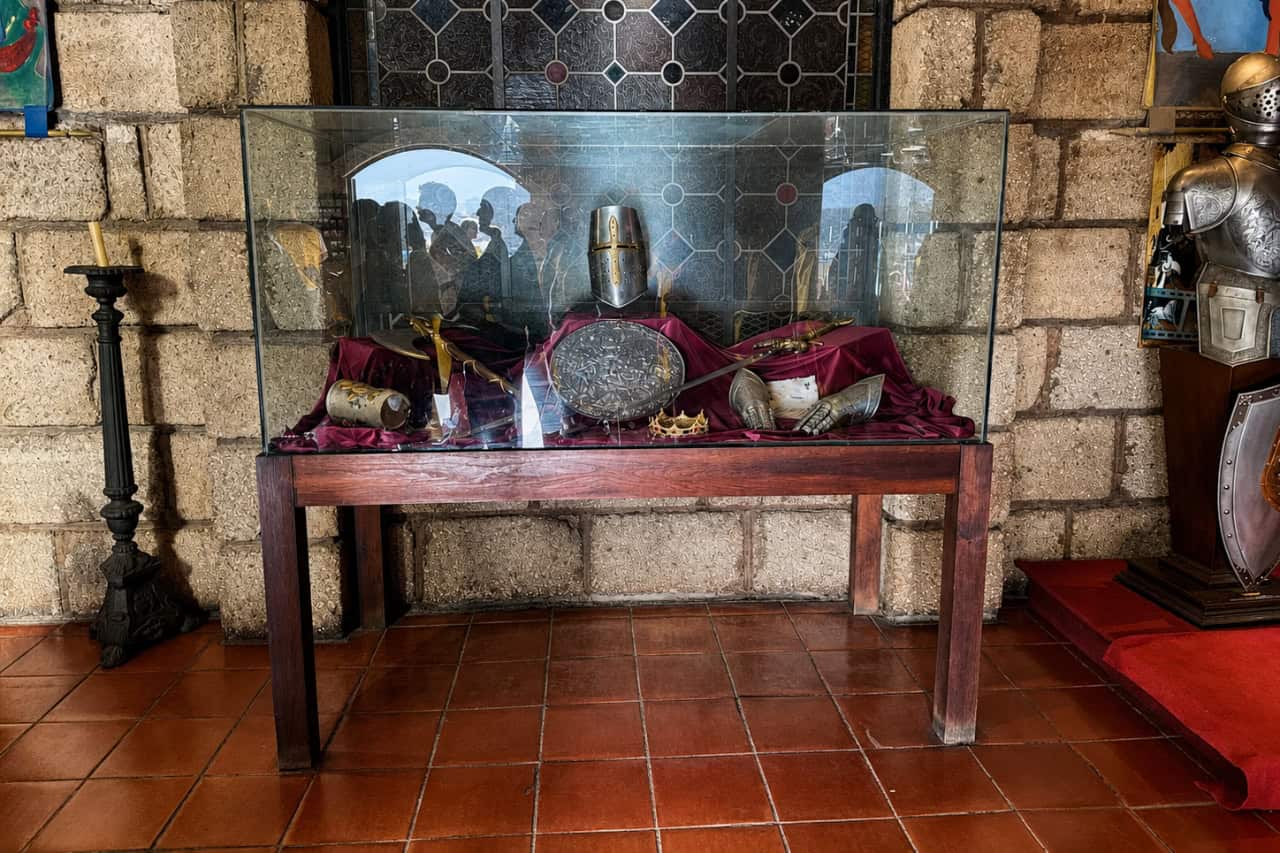 Helmet, shield, sword, gauntlets and crown displayed behind glass at a medieval dinner show Tenerife venue.