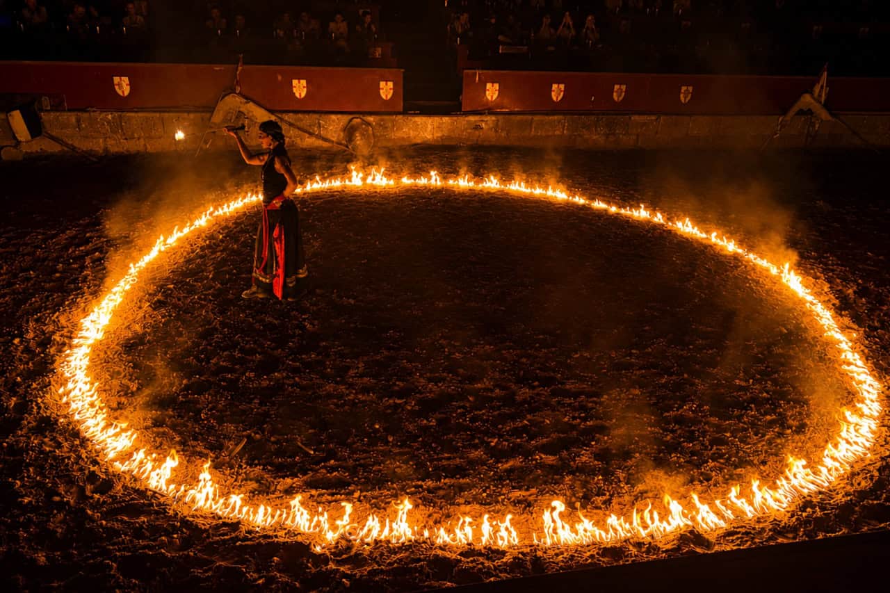 Performer stands inside a large ring of fire during a medieval show south Tenerife arena sequence.