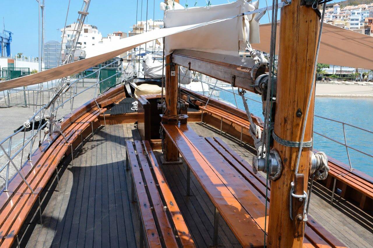 The spacious wooden deck of the Peter Pan sailing boat in Los Cristianos, with long bench seating, a large shade canopy, traditional masts and rigging, and open space for guests to relax during the Tenerife boat trip.