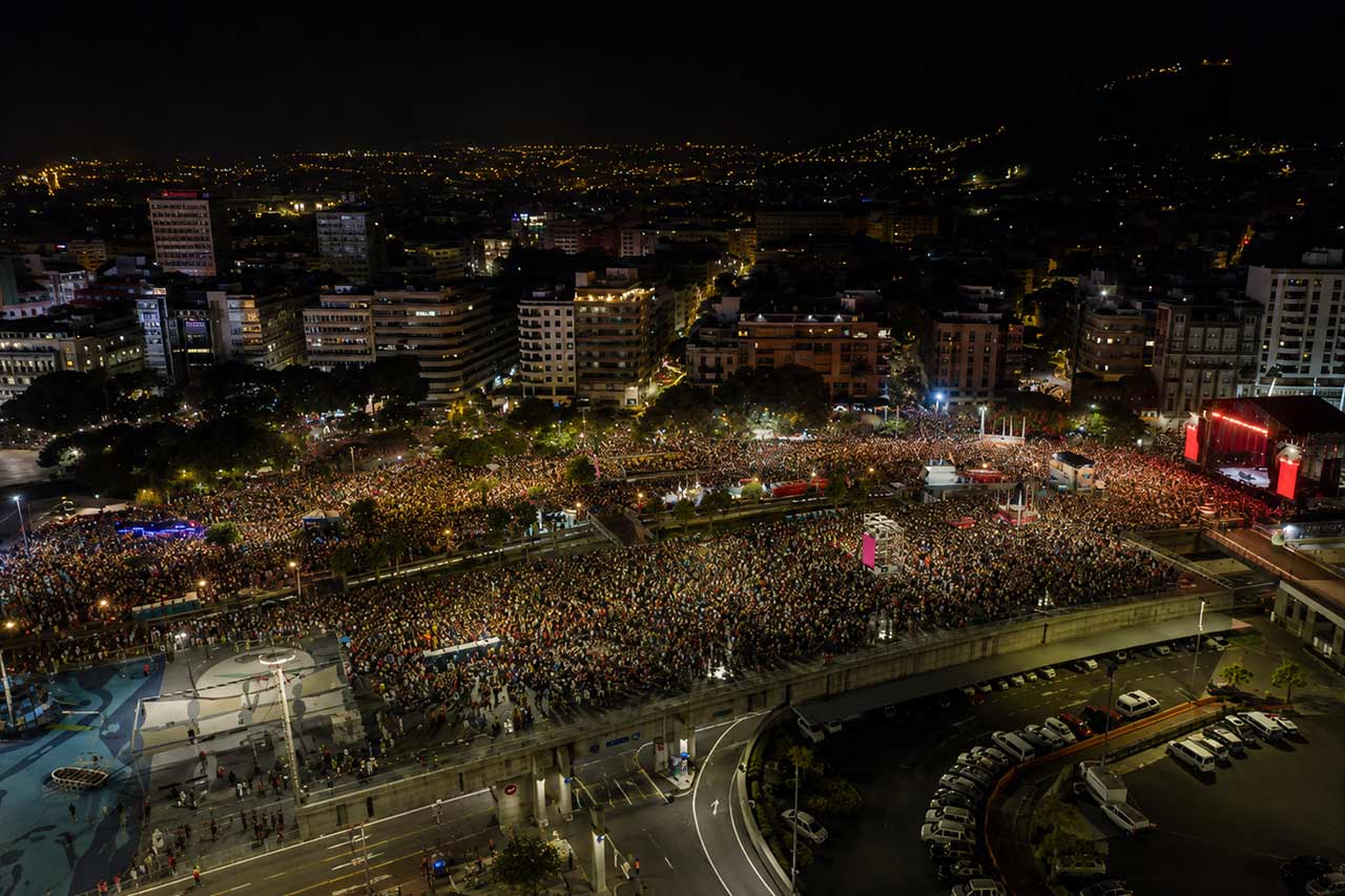 Miles de personas llenan las calles de Santa Cruz de Tenerife durante una ajetreada noche de celebración del Carnaval. Disfraces coloridos, decoraciones iluminadas, puestos de comida y bebida, música y aglomeraciones transforman el centro de la ciudad en una enorme fiesta al aire libre, mostrando la magnitud y el ambiente nocturno del Carnaval de Tenerife.