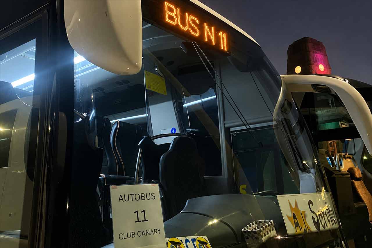 Nocny transport autokarowy dla gości biorących udział w karnawale w Santa Cruz de Tenerife. Na zdjęciu widoczny jest nowoczesny autobus oznaczony symbolem Club Canary, przeznaczony dla pasażerów, a w tle rozświetlone miasto – symbolizujące zorganizowany transport i wygodne przejazdy do i ze słynnych obchodów karnawału na Teneryfie.