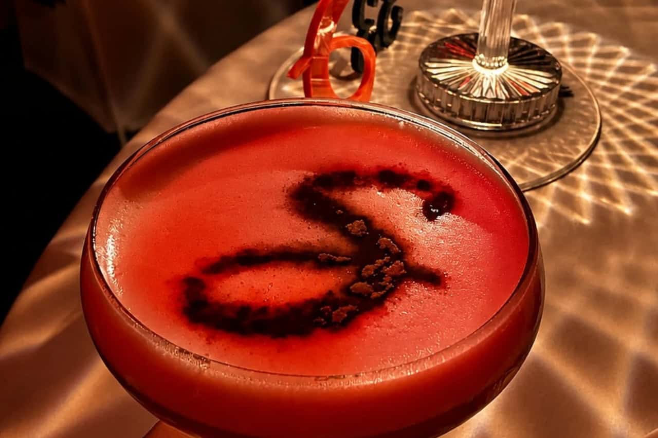 Red cocktail in a coupe glass with dark decorative swirls at a cabaret dinner show Tenerife.