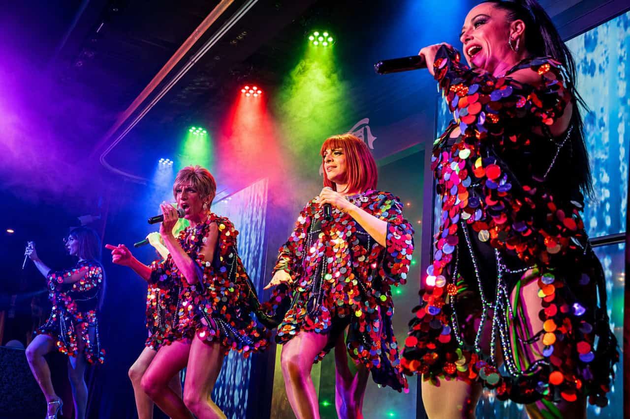 Drag performers singing in colourful costumes under bright lights