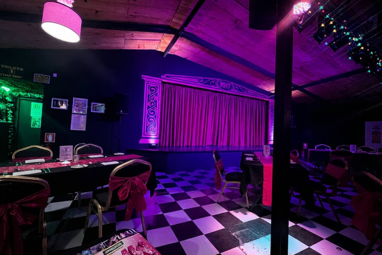 The MHT venue with curtained stage and dining tables under purple light