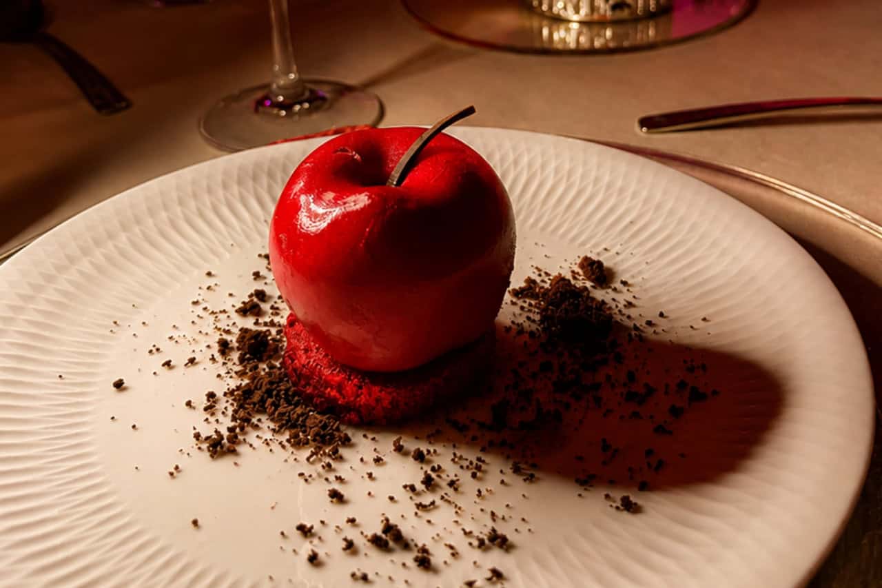 Example of a glossy red apple-shaped dessert served as a plated course at the Scandal Dinner Show.