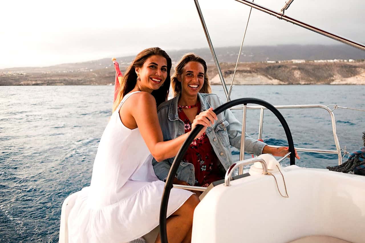 Two guests smile at the helm while enjoying the Atlantic Star small-group sailing and whale-watching experience in Tenerife.
