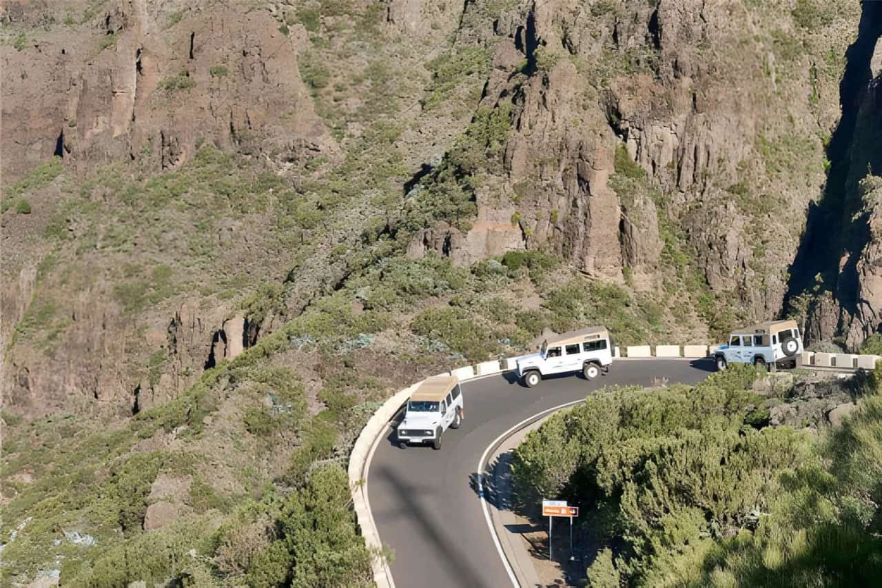 Safari jeeps travelling beneath dramatic cliffs during a La Gomera excursion from Tenerife