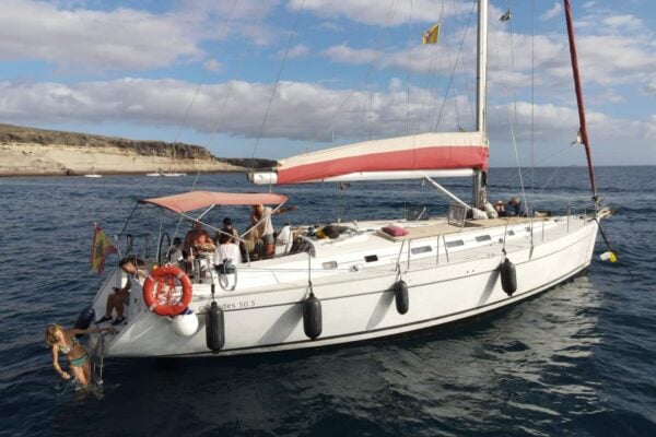 Small group whale watching sailing boat in Tenerife anchored by the coast with guests swimming off the back