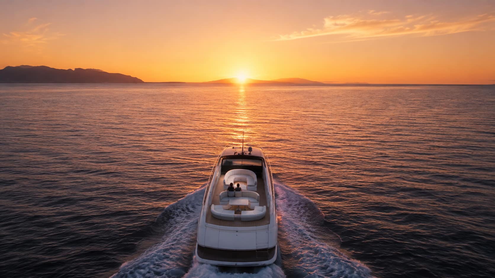 Seaduction cruising across the calm Atlantic Ocean at sunset, with two guests relaxing on the rear deck as the yacht sails toward the glowing horizon and distant islands near Tenerife.