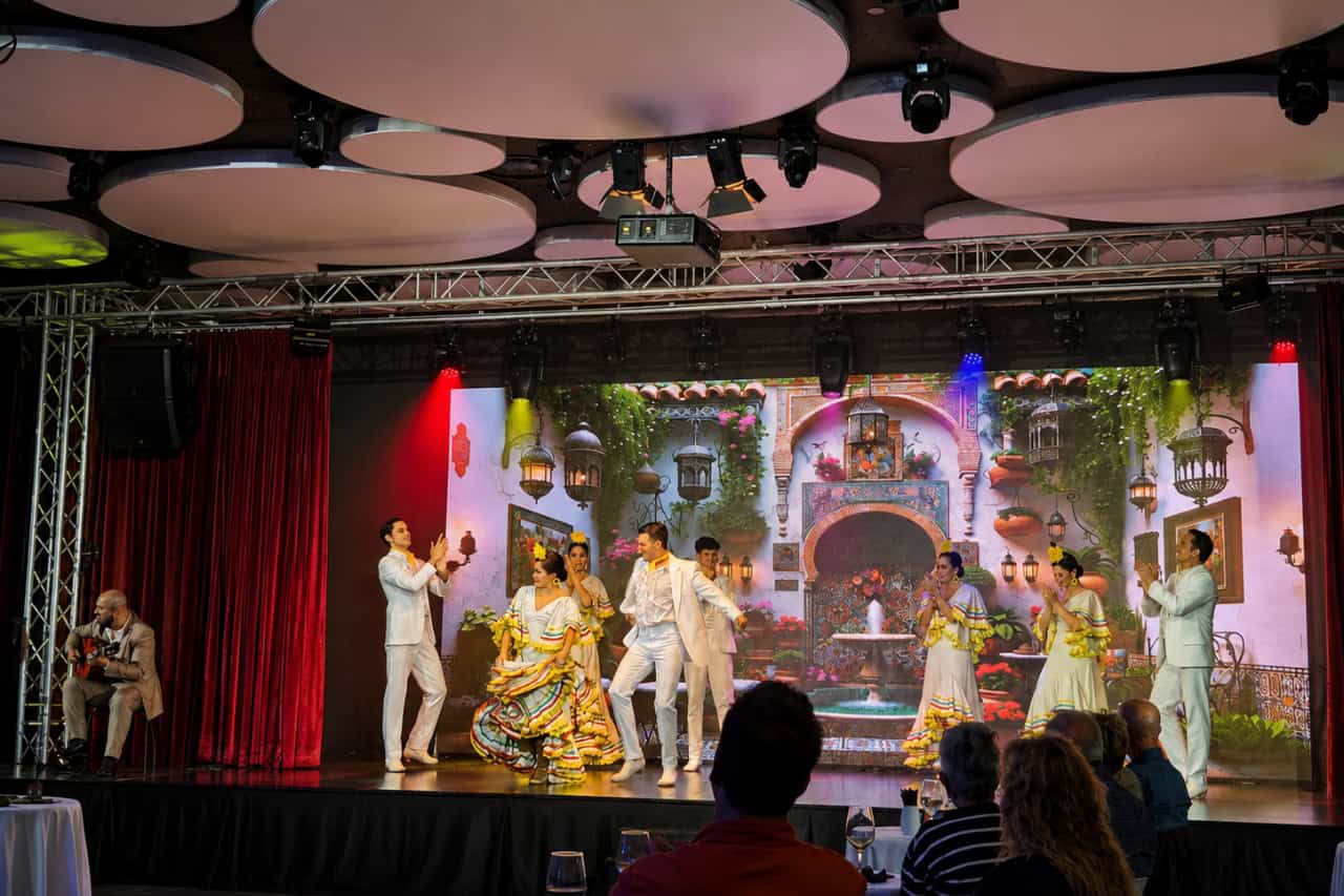 A seated guitarist plays beside dancers in white costumes during live flamenco guitar Tenerife.