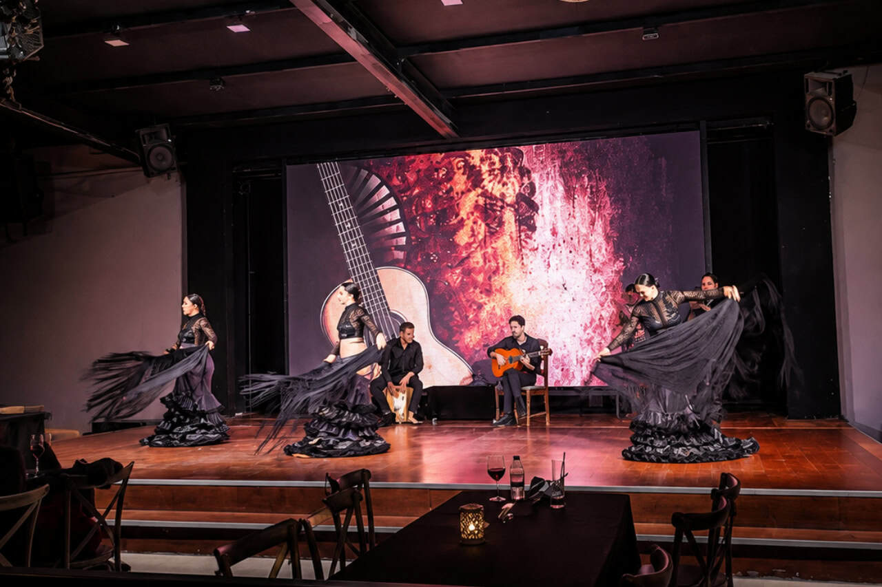 Three dancers in black skirts perform beside a guitarist and percussionist during live flamenco Tenerife.