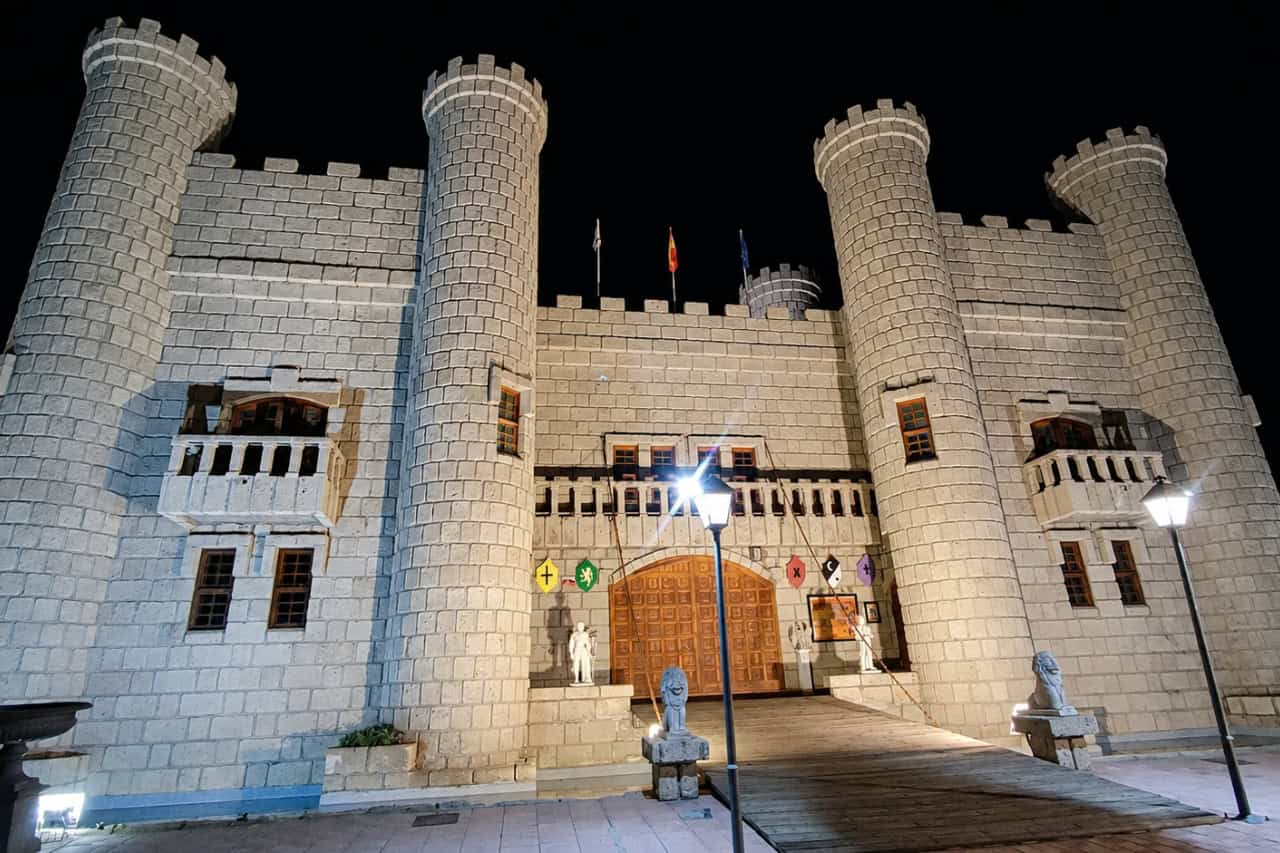 Stone castle-style exterior at night with lit towers, flags and a wooden entrance at Theatre Coliseo Tenerife.