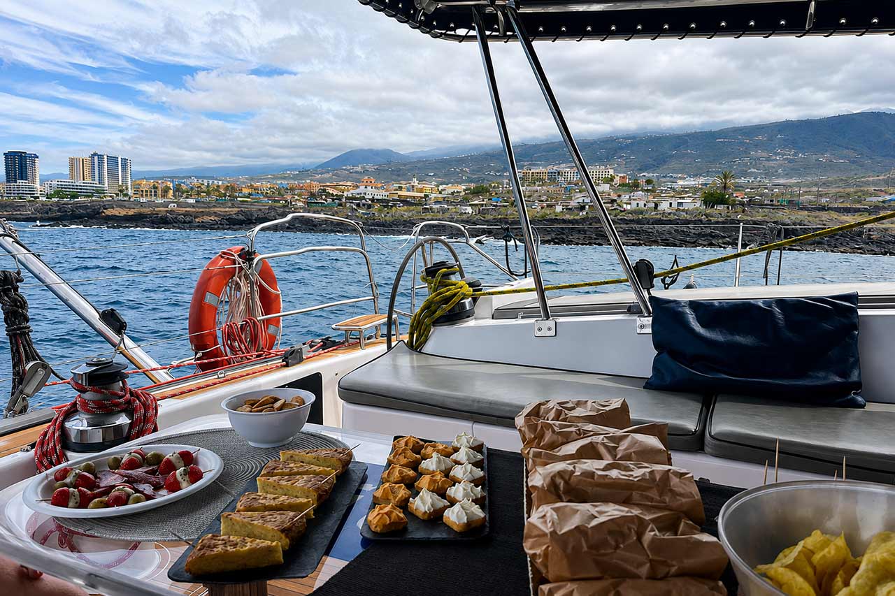 Snacks en versnaperingen bereid aan boord van de Abrazo terwijl gasten genieten van het uitzicht op de kustlijn van Tenerife vanaf de catamaran