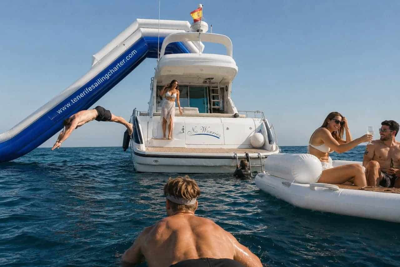 Guests enjoying a luxury day at sea aboard the No Worries Yacht in Tenerife, relaxing on floating loungers, swimming in crystal-clear waters, and using the yacht’s inflatable slide during a private yacht charter experience.