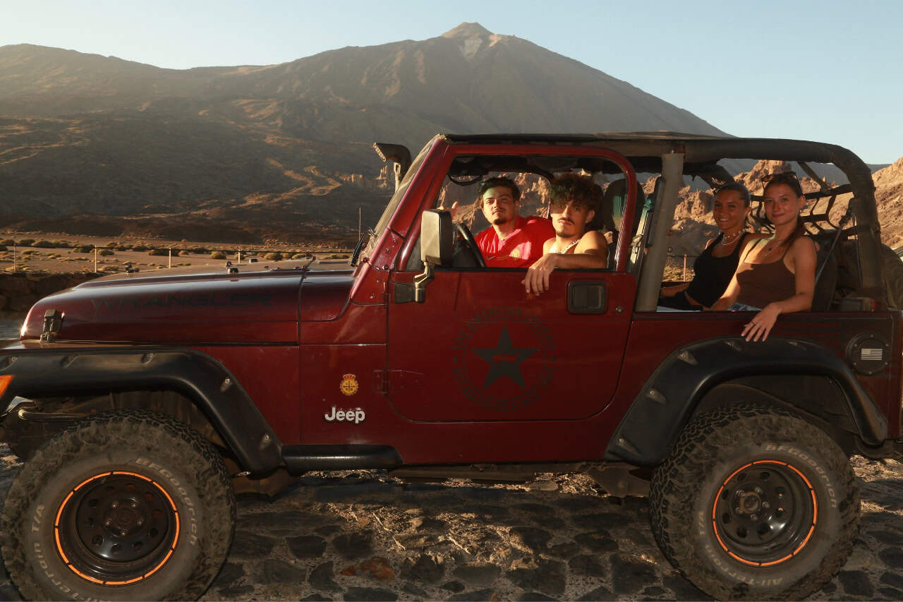 A red jeep with a group of friends inside neext to the mountains