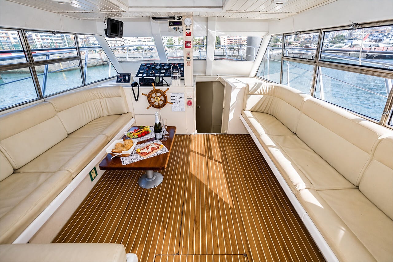 Neptuno’s spacious indoor lounge with comfortable cream seating, large panoramic windows, a wooden floor and a shaded area where guests can relax during the boat trip.