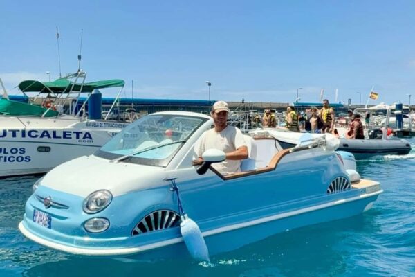 Un hombre sonriente conduciendo una lancha Fiat-500 de color azul brillante en las cristalinas aguas de Tenerife