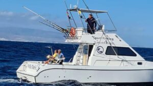 Seitenansicht eines weißen Sportfischerboots mit dem Namen "Sport Fishing", das auf dem Meer fährt, mit zwei älteren Menschen, die aktiv fischen, und einer jüngeren Person, die das Boot steuert