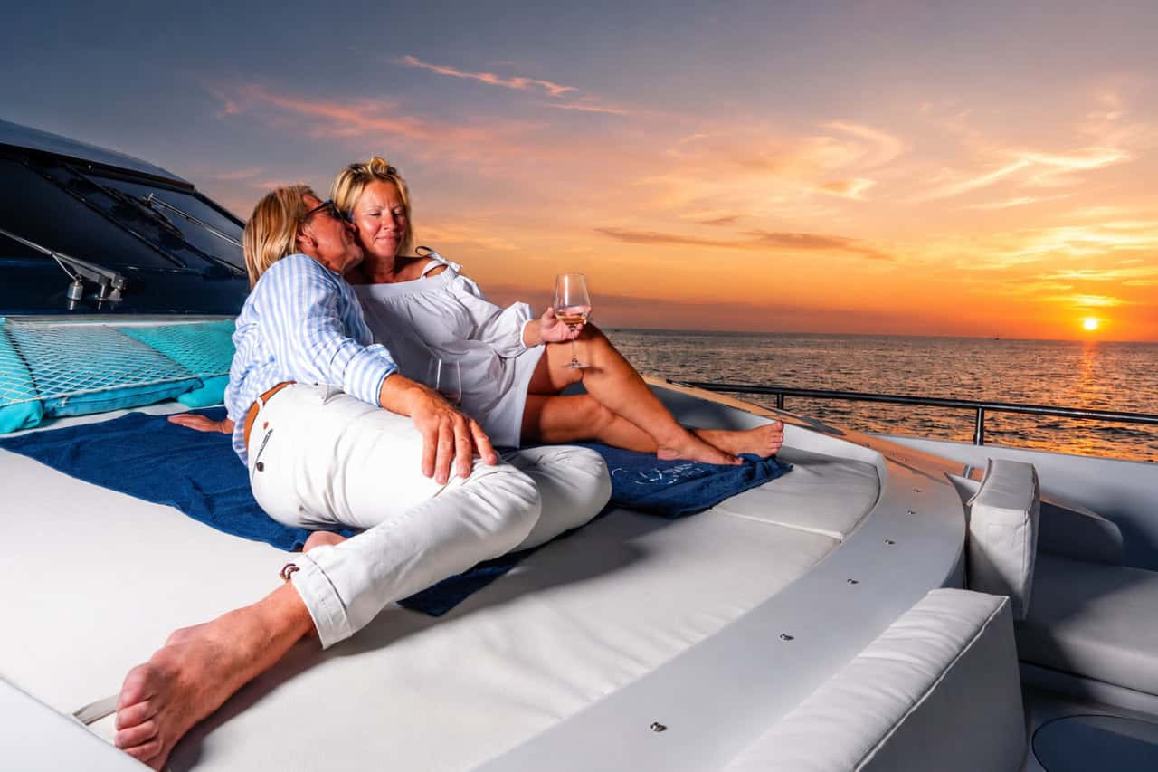 Couple relaxing with wine on the front deck of a luxury yacht during a private sunset cruise in Tenerife, surrounded by golden skies and calm ocean views, creating the perfect romantic setting for a marriage proposal.