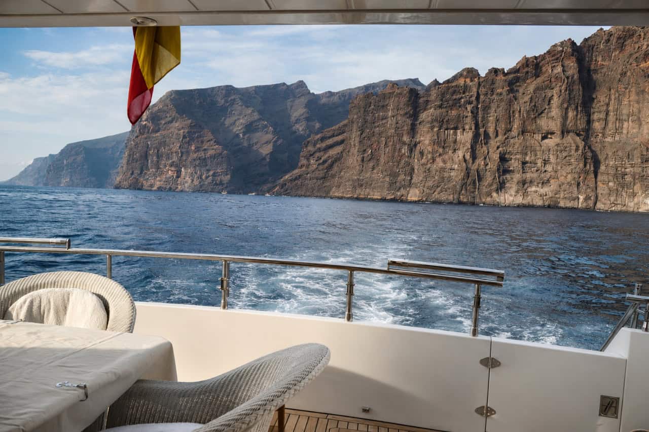 Outdoor dining table prepared aboard the Rockstar yacht with Tenerife's volcanic coastline and lighthouse in the background.