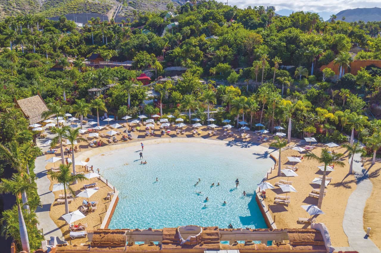 Calm pool with sandy beach and palm trees at Siam Park