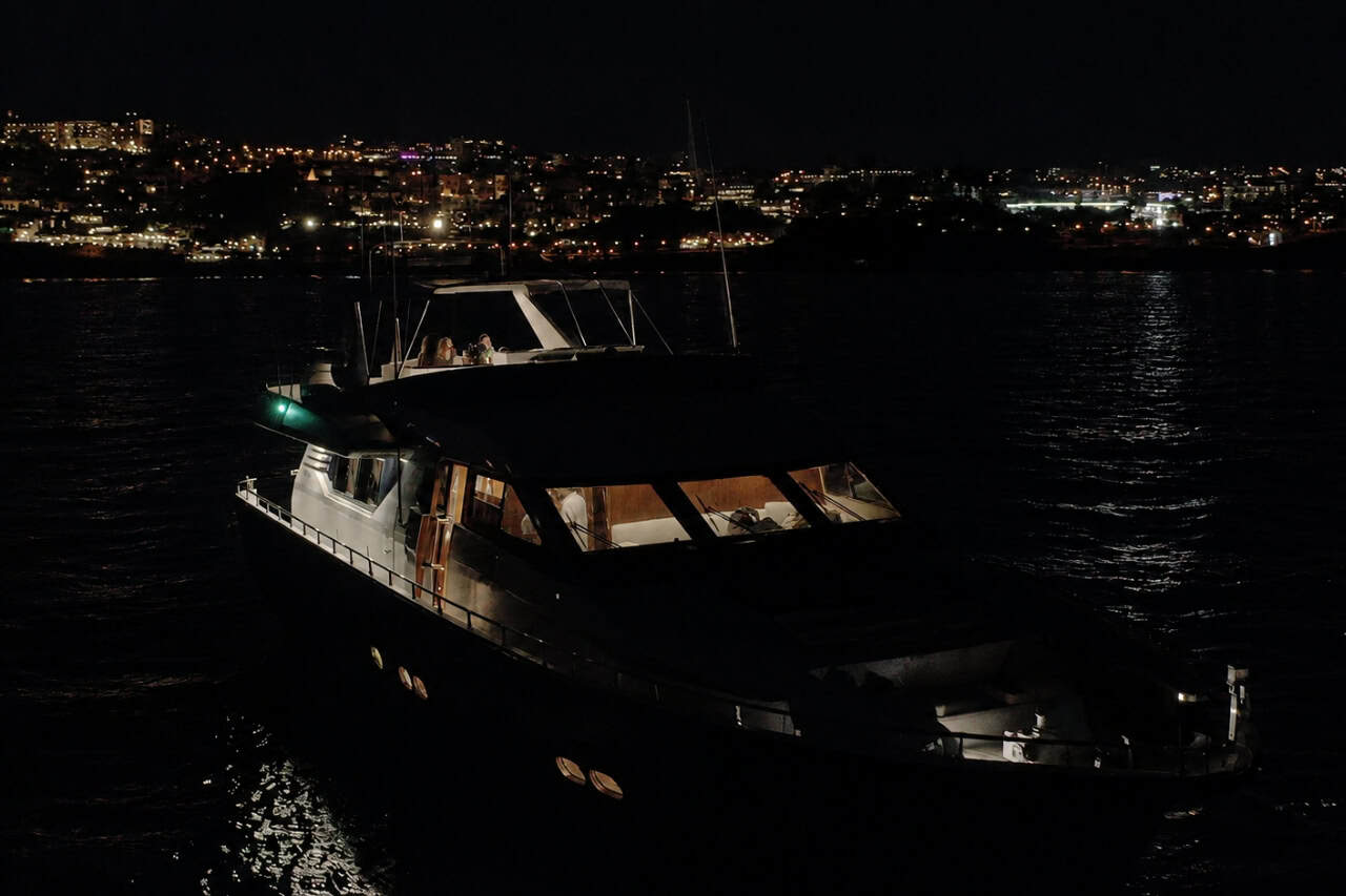 Private yacht cruising along the illuminated Tenerife coastline at night during a yacht dinner party and evening dining experience on the ocean.