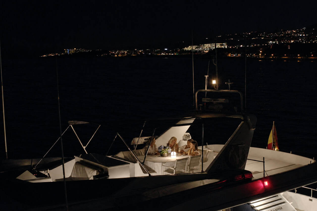 Guests enjoying a private yacht dinner experience in Tenerife on the upper deck, with a candlelit table and the island lights visible in the distance.