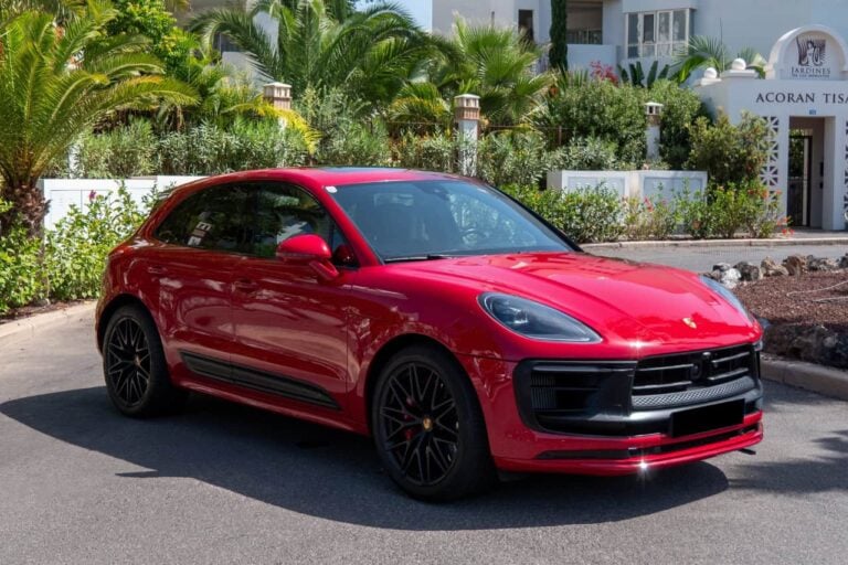 Porsche Macan GTS roșu din unghiul lateral frontal, evidențiind farurile sportive, jantele negre și designul aerodinamic.