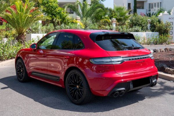 Sarkanais Porsche Macan GTS novietots ārā ar palmām fonā, parādot tā gludo aizmugures dizainu un četras izplūdes caurules.