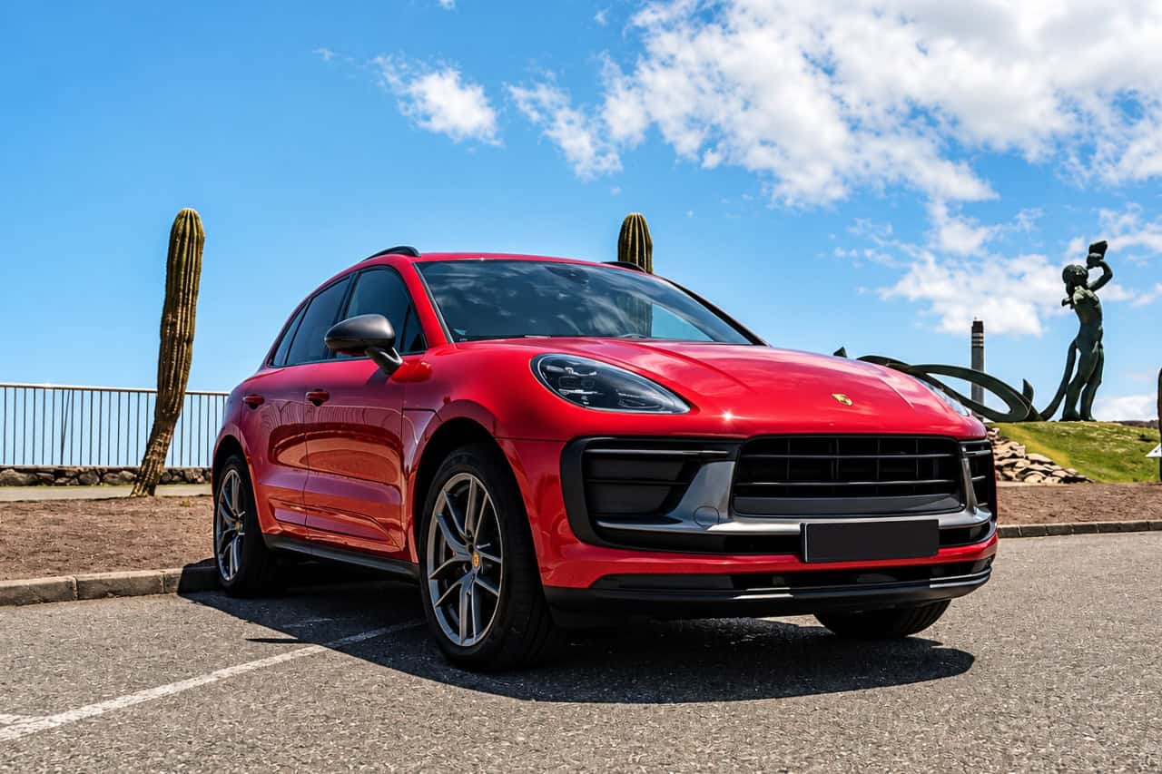 Art de la carte de la Porsche Macan à louer à Tenerife, Macan rouge garée au bord de la mer sous un ciel bleu