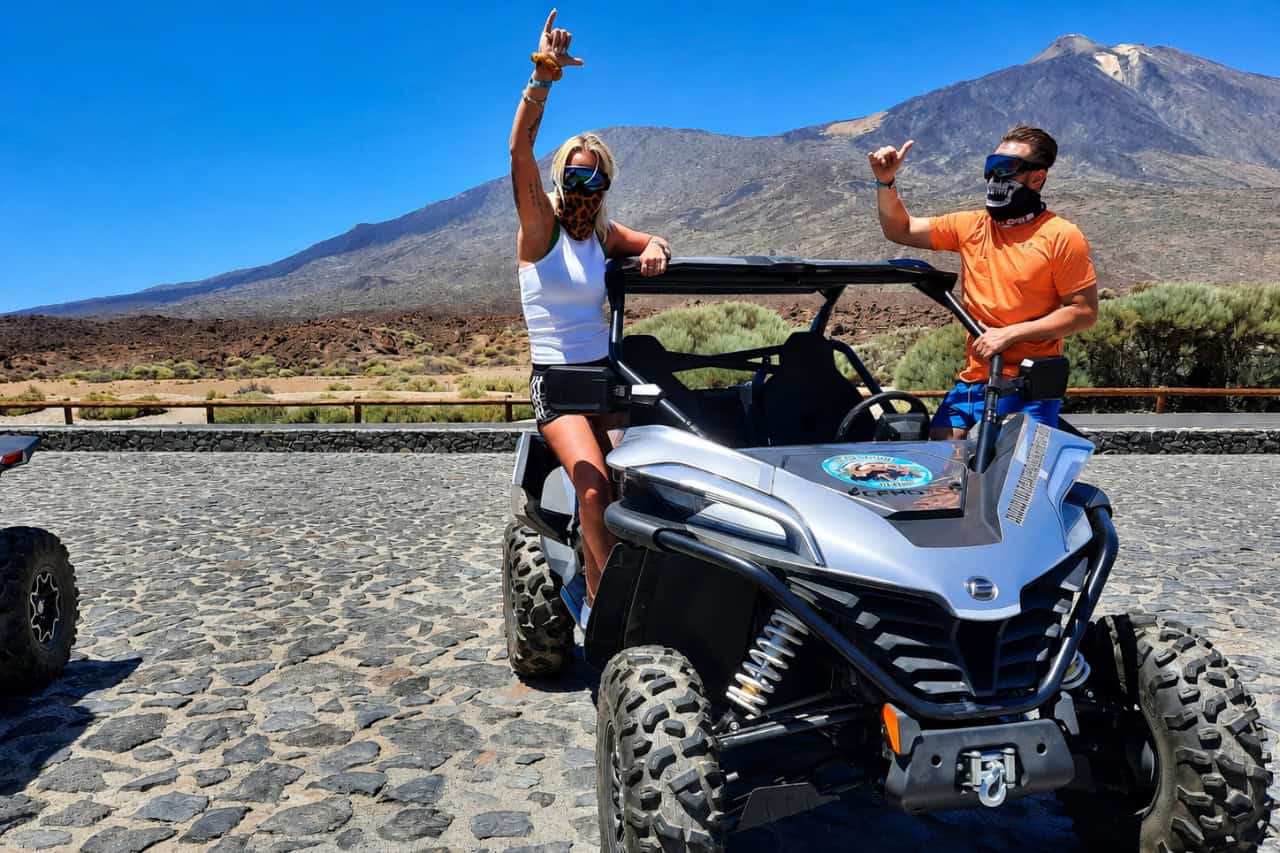 Two visitors posing with an off-road buggy in front of Mount Teide during a Tenerife adventure tour.