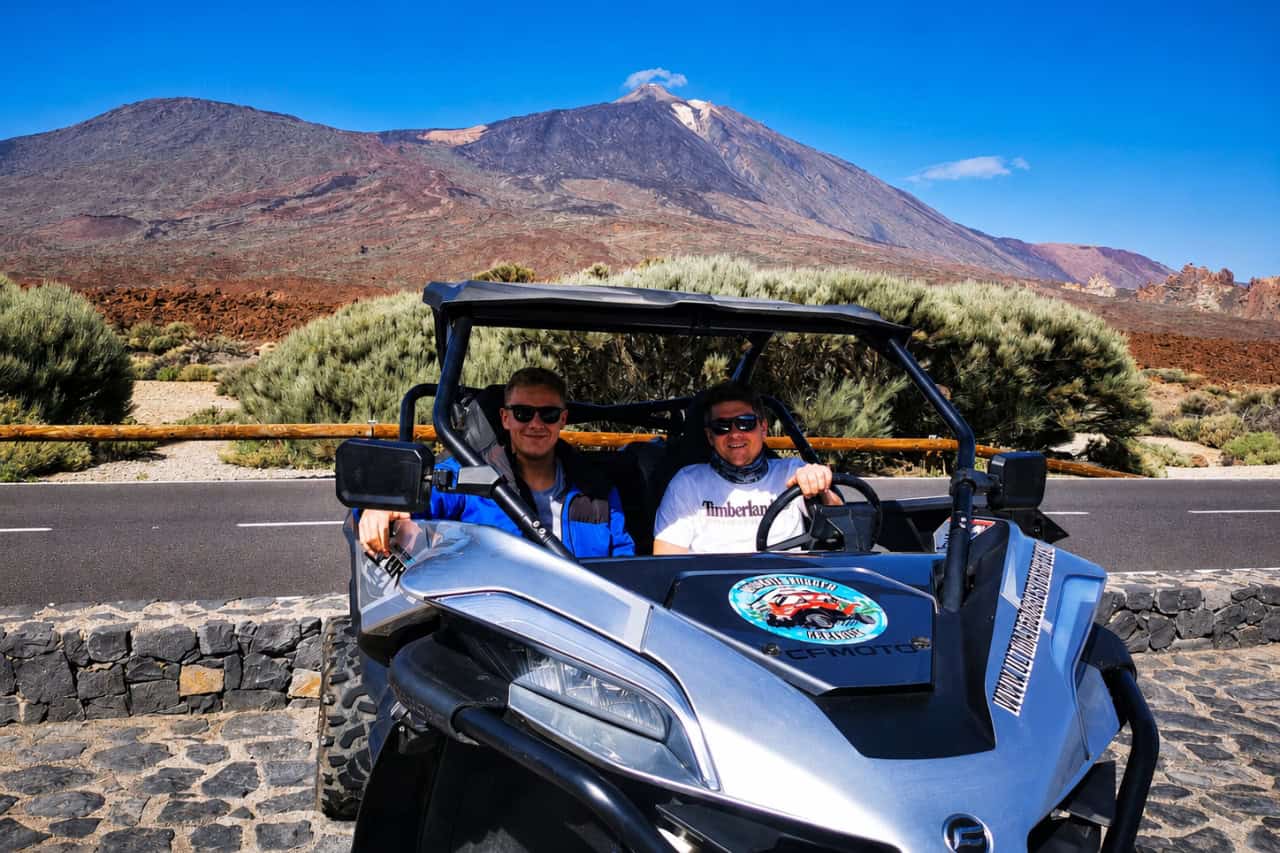Two riders sitting in a buggy with Mount Teide and volcanic scenery in the background.