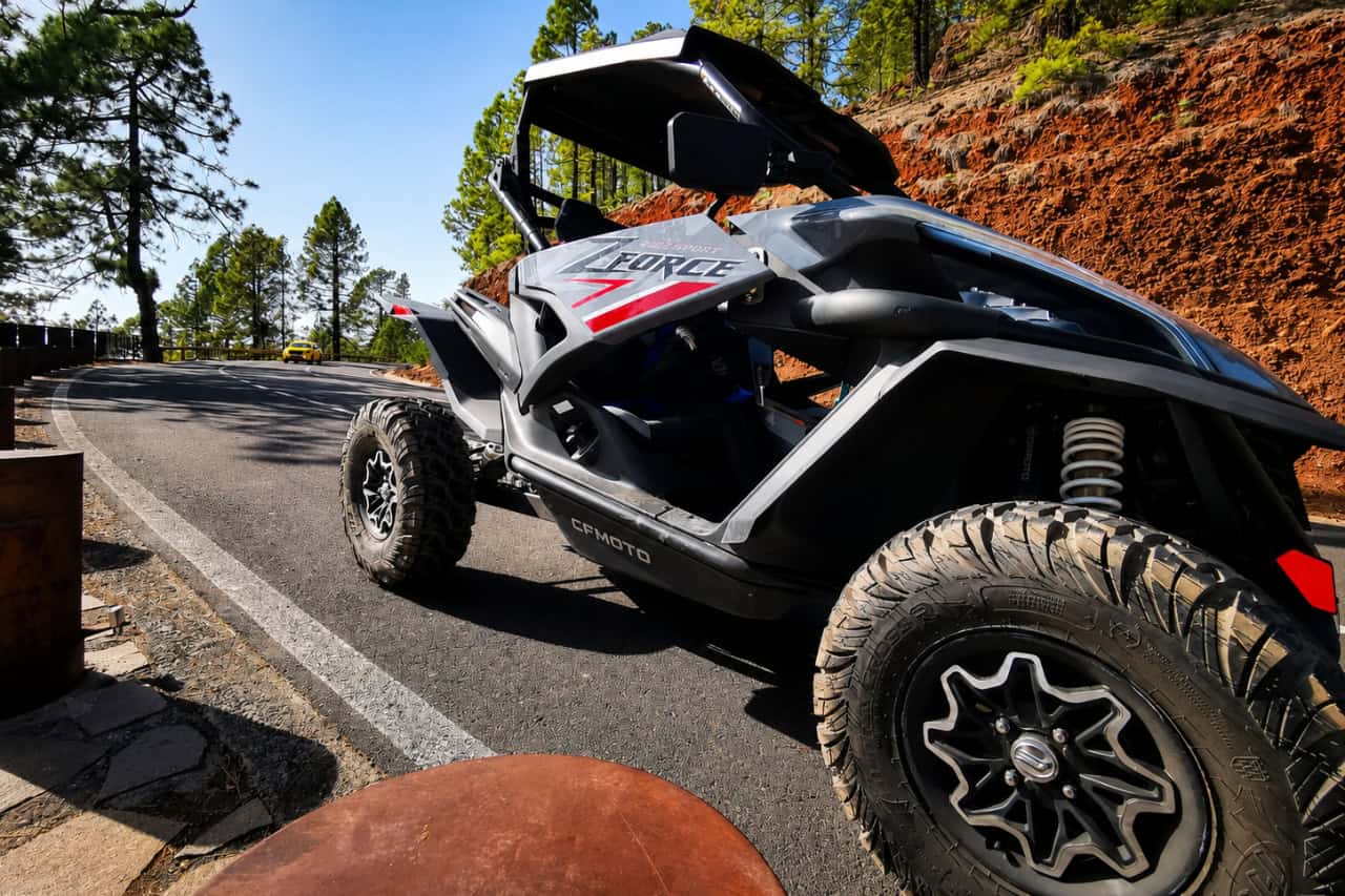 CFMOTO ZForce buggy parked beside a winding mountain road surrounded by pine forest in Tenerife.