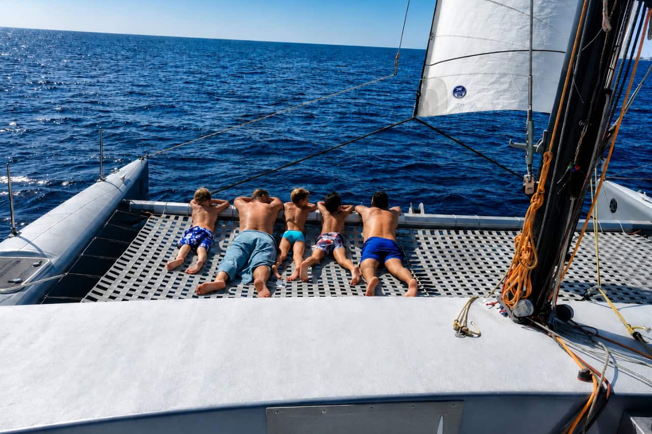 Adult and children relaxing on the front net of a sailing catamaran overlooking the open ocean