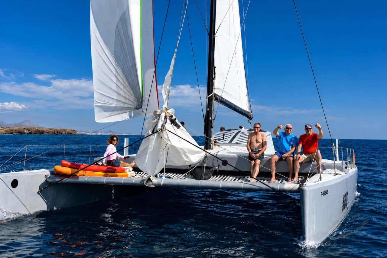 Sailing catamaran viewed from the water with guests relaxing on board beneath bright afternoon sunlight