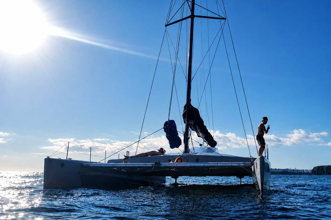 Sailing catamaran viewed from the water with guests relaxing on board beneath bright afternoon sunlight
