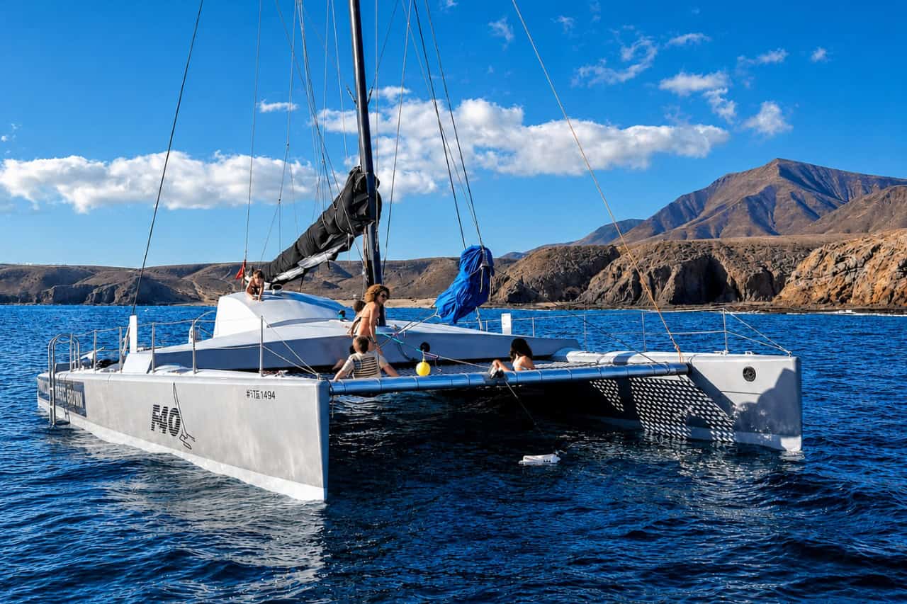 White sailing catamaran with guests on board near the rugged volcanic coastline of Lanzarote