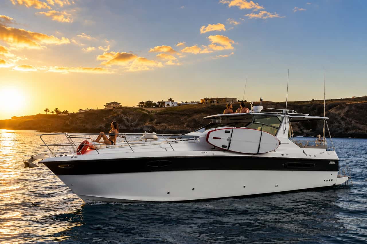 White luxury motor yacht cruising near the Lanzarote coastline during a golden sunset with guests relaxing on deck